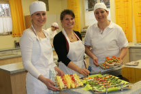 Drei Frauen mit Küchenschürzen stehen vor Platten mit Häppchen