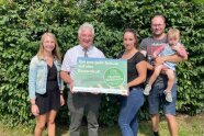 Gruppenfoto mit Behördenleiter vor einer Hecke mit Schildübergabe