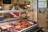 Verkäuferin steht hinter einer Wursttheke und schneidet eine Wurst