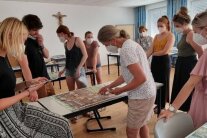 Personen stehen um einen Tisch und blicken auf ein Spielbrett
